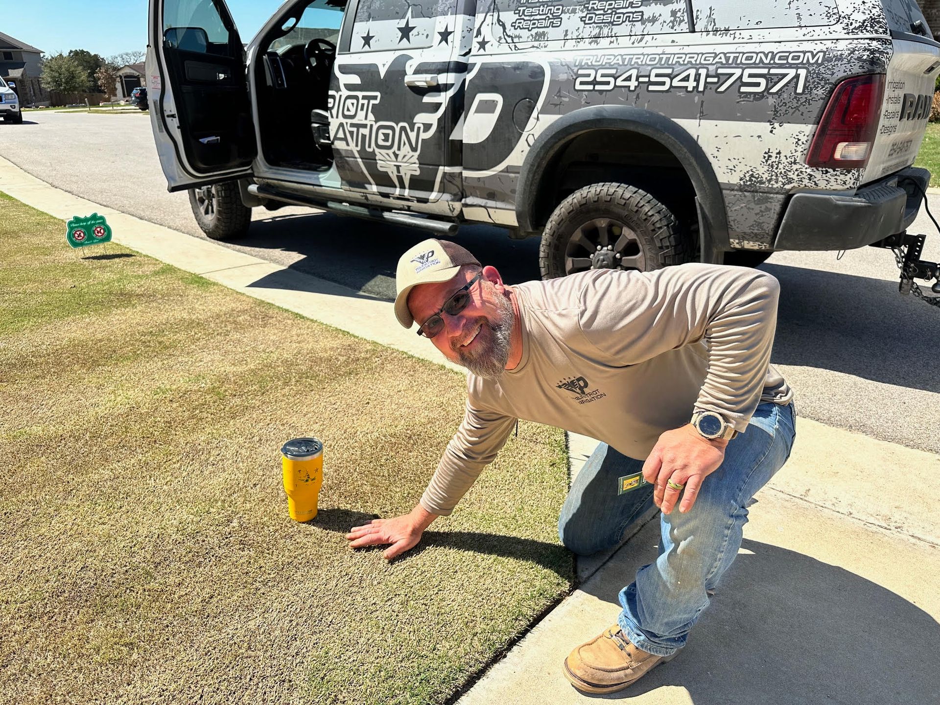 A man is kneeling on the sidewalk in front of a truck.