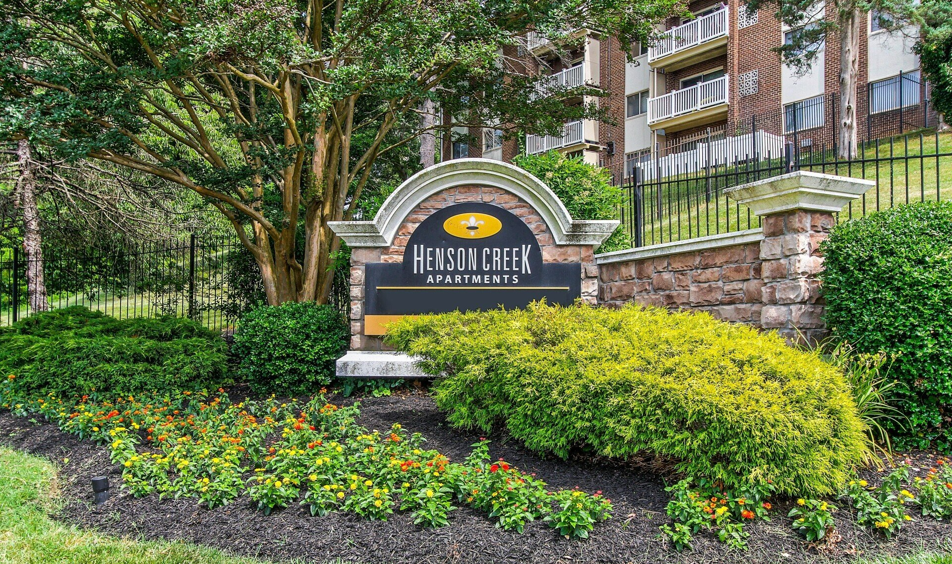 Stone entrance sign for Henley at Riverfront, surrounded by green shrubs and trees in front of apartments