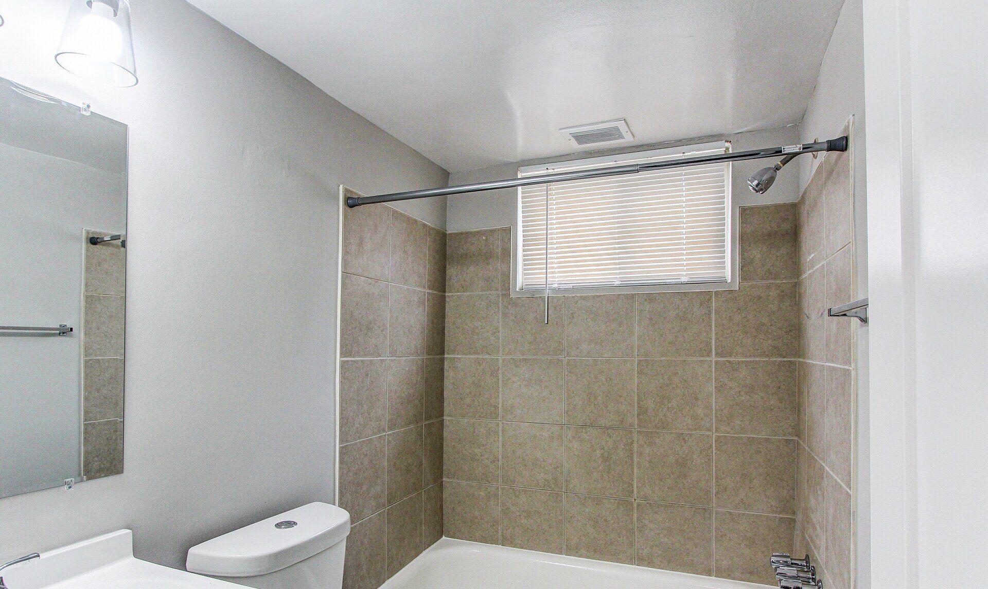 Bright bathroom shower with tan tile walls, white shower curtain, and a toilet beside it