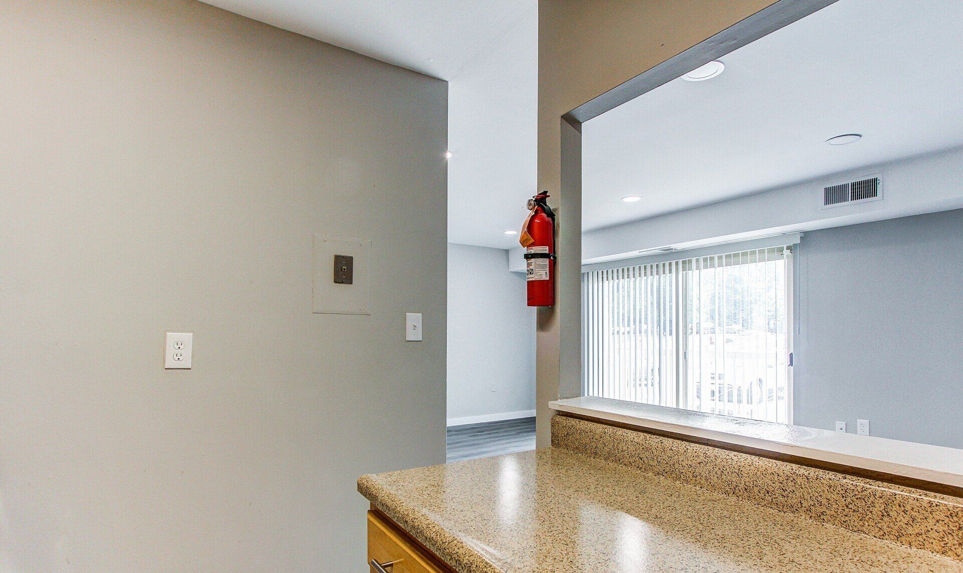 Empty kitchen interior with granite counter, gray walls, and a red fire extinguisher near the doorway