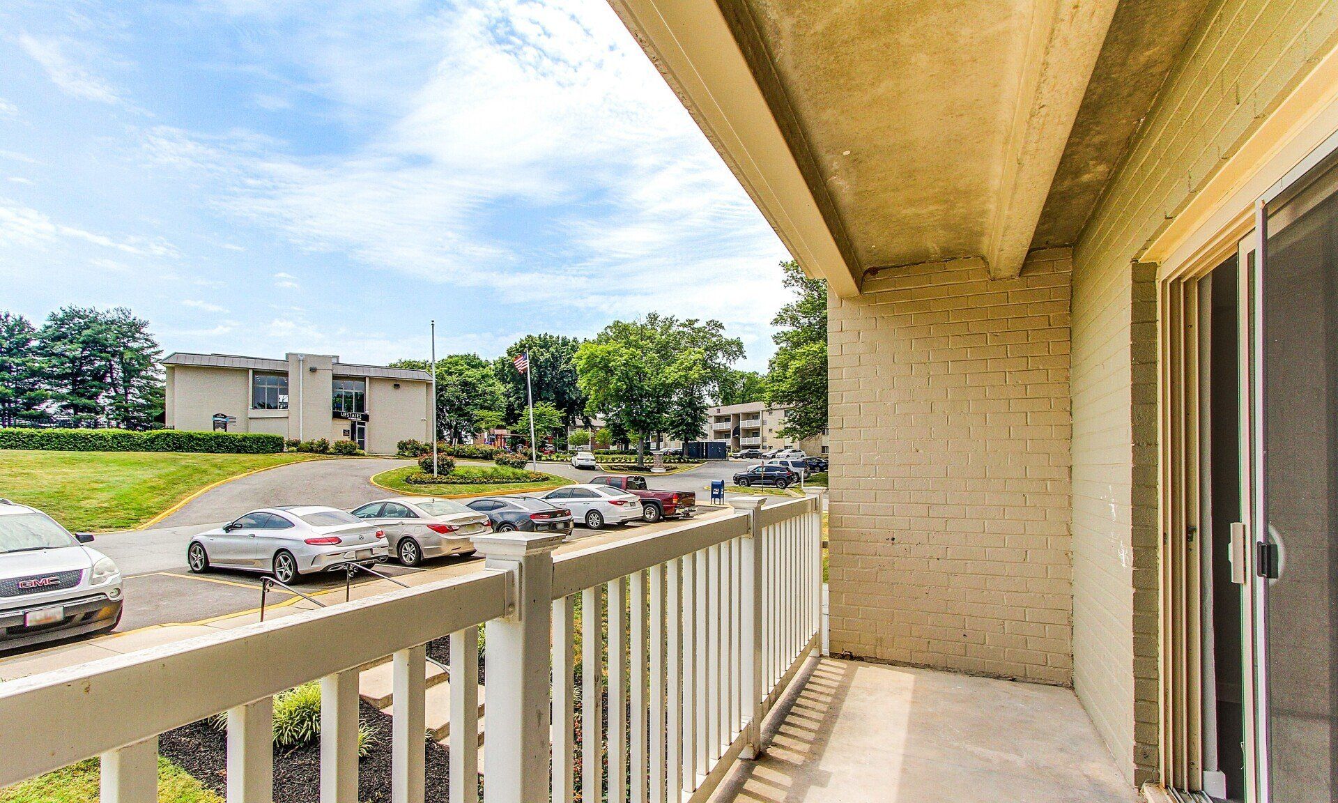 Apartment balcony overlooking a parking lot and trees on a sunny day