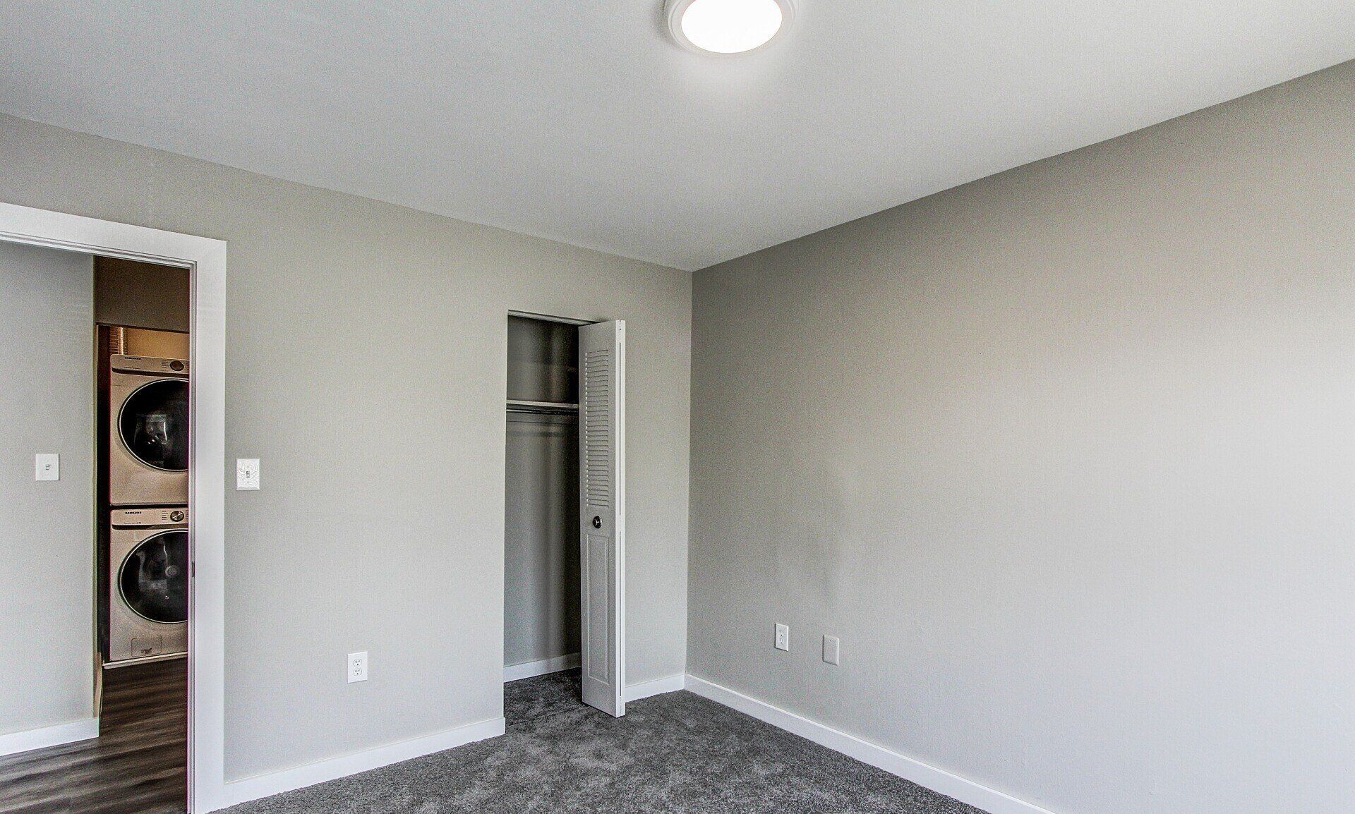 Empty gray bedroom with open closet and carpeted floor