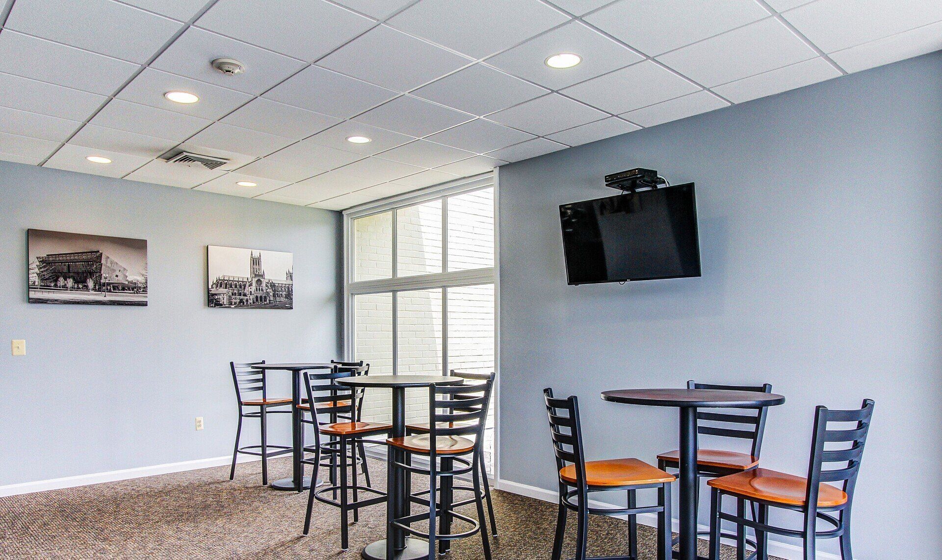 Quiet café seating area with tables, chairs, wall art, and a mounted TV in a bright room.