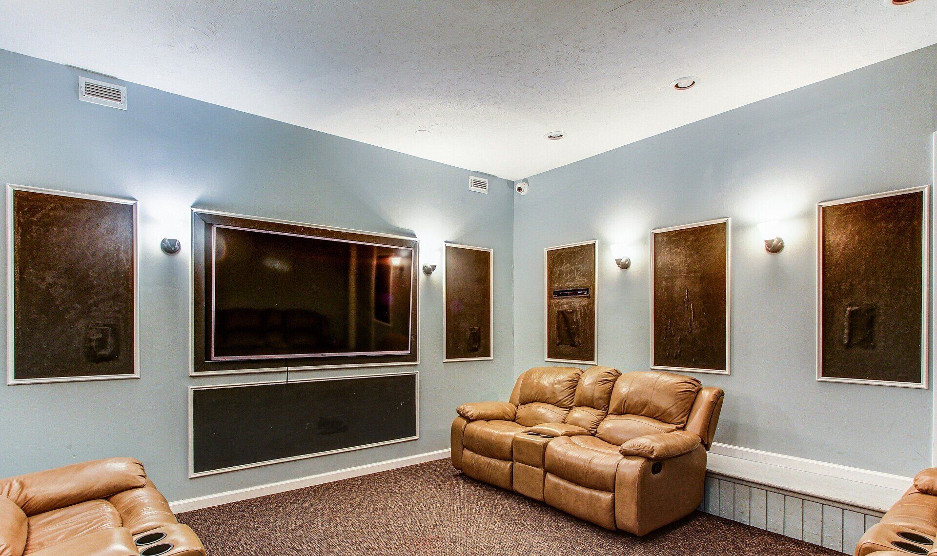 Media room with wall-mounted TV, leather recliners, gray walls, and framed posters