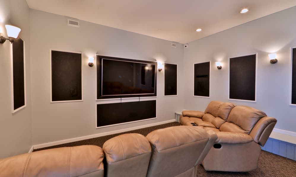 Modern living room with gray sectional sofa and wall-mounted TV surrounded by black acoustic panels.