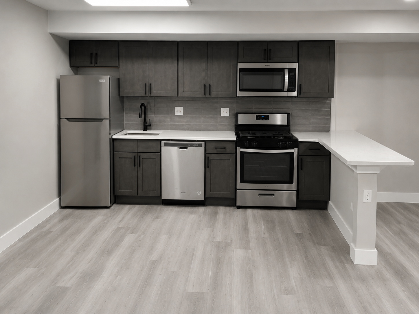 Modern kitchen with dark cabinets, stainless appliances, and a white breakfast bar￼