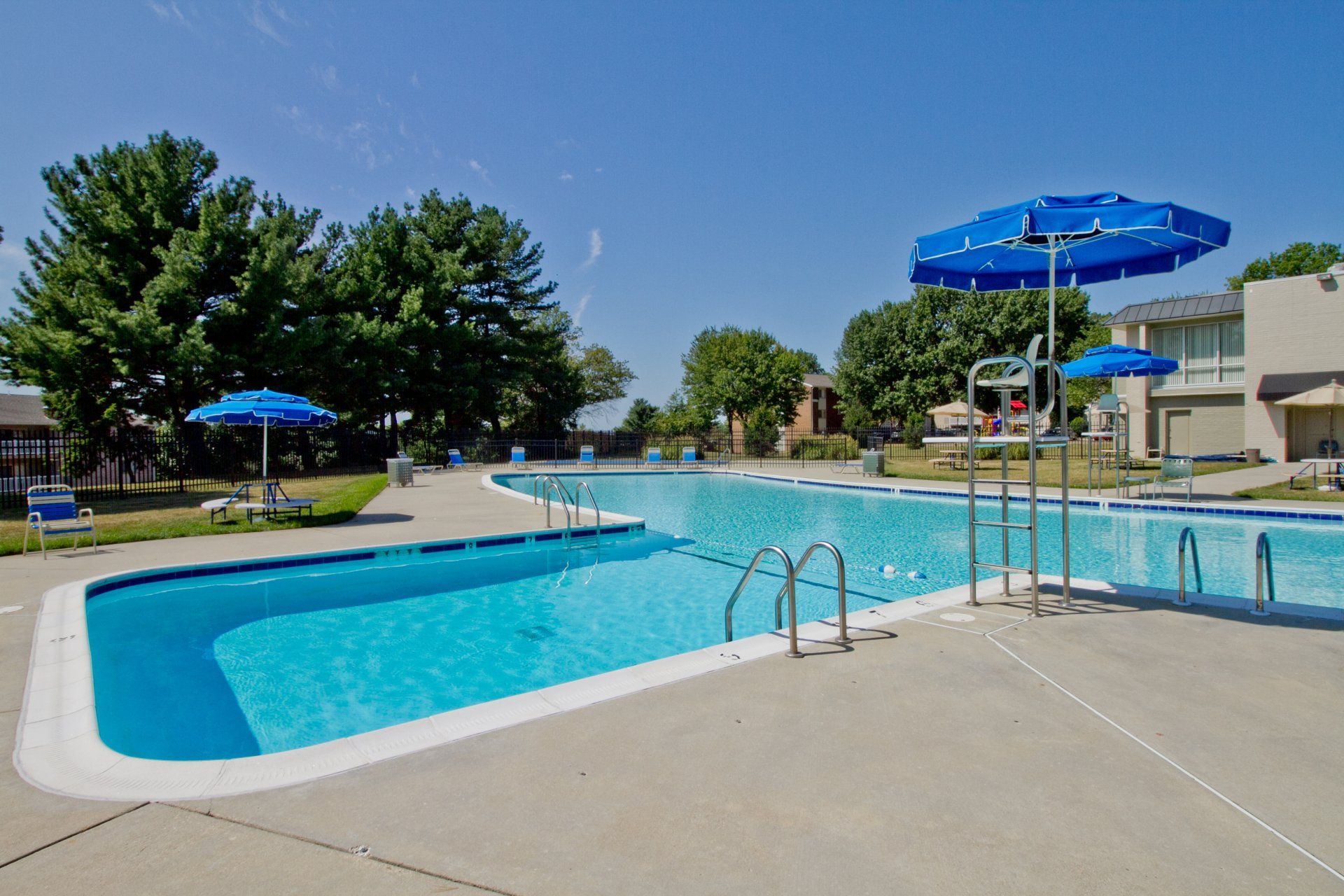 Outdoor swimming pool with blue umbrellas, lounge chairs, and clear water on a sunny day