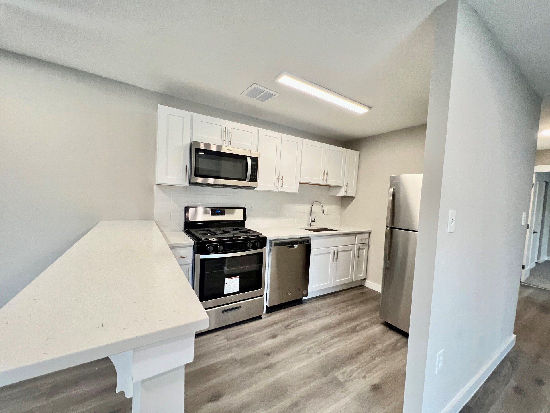 Small modern kitchen with white cabinets, stainless appliances, and gray wood-look flooring