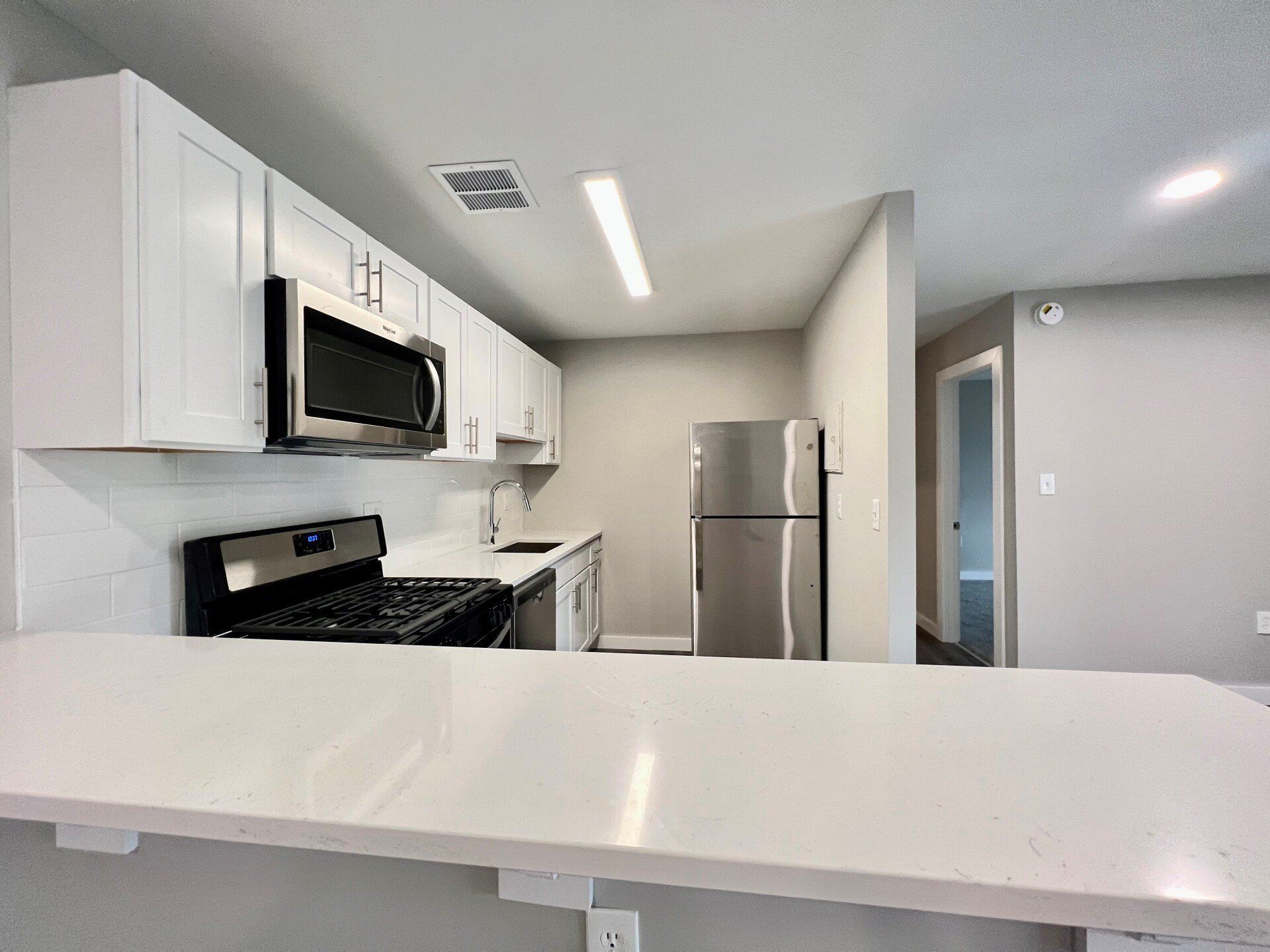 Modern kitchen with white cabinets, black appliances, stainless fridge, and a large white countertop