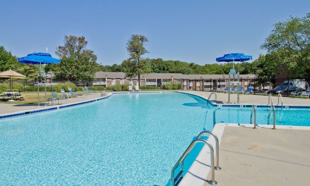 Outdoor swimming pool with bright blue umbrellas and a metal ladder on a sunny day
