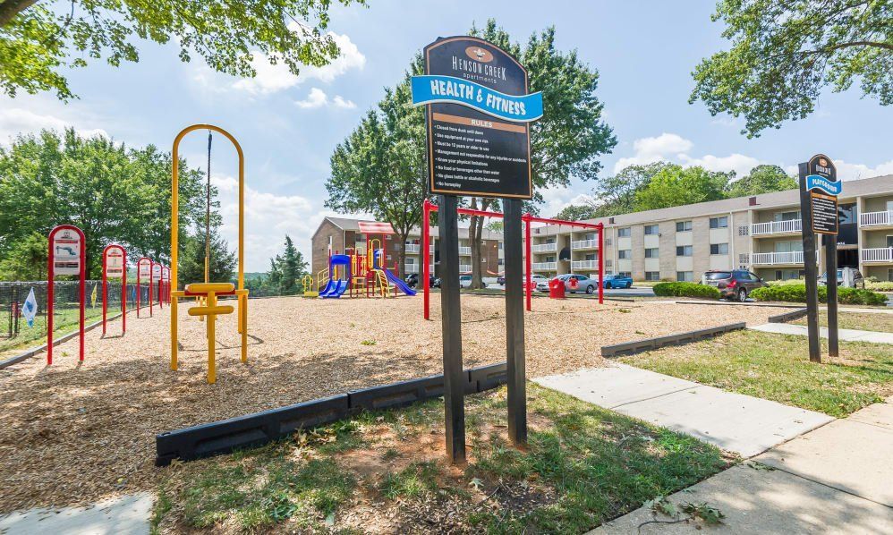 Playground with red climbing bars, mulch ground, and a sign at an apartment complex on a sunny day