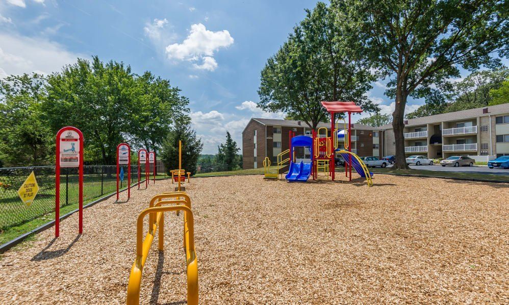 Colorful playground with slides and climbing structures on a woodchip surface beside apartment buildings and trees