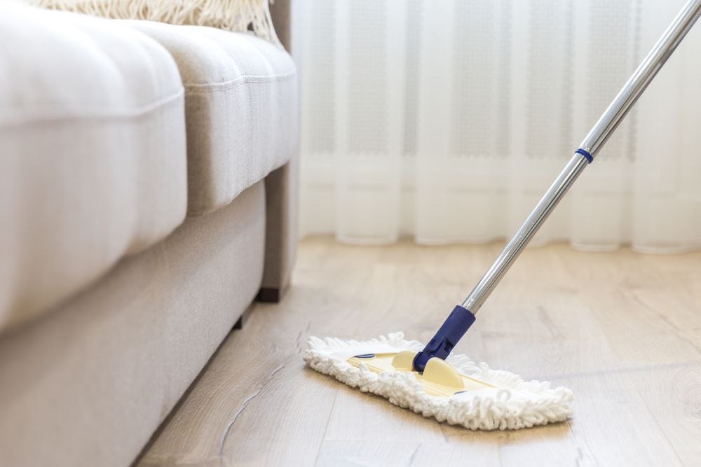 A Mop Is Sitting On A Wooden Floor In A Living Room Next To A Couch — Wyong Commercial Cleaning In Wyongah, NSW