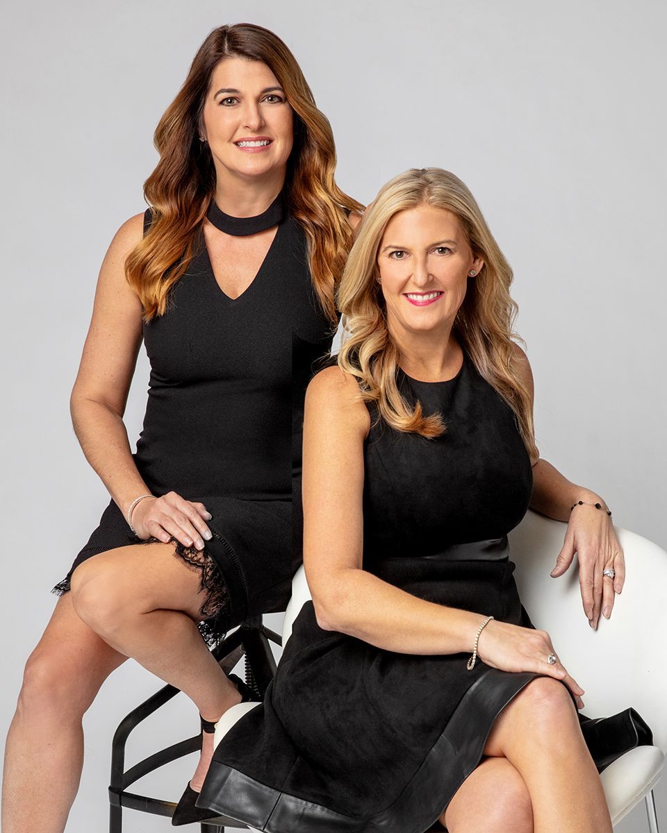Two women in black dresses are sitting next to each other on a chair.