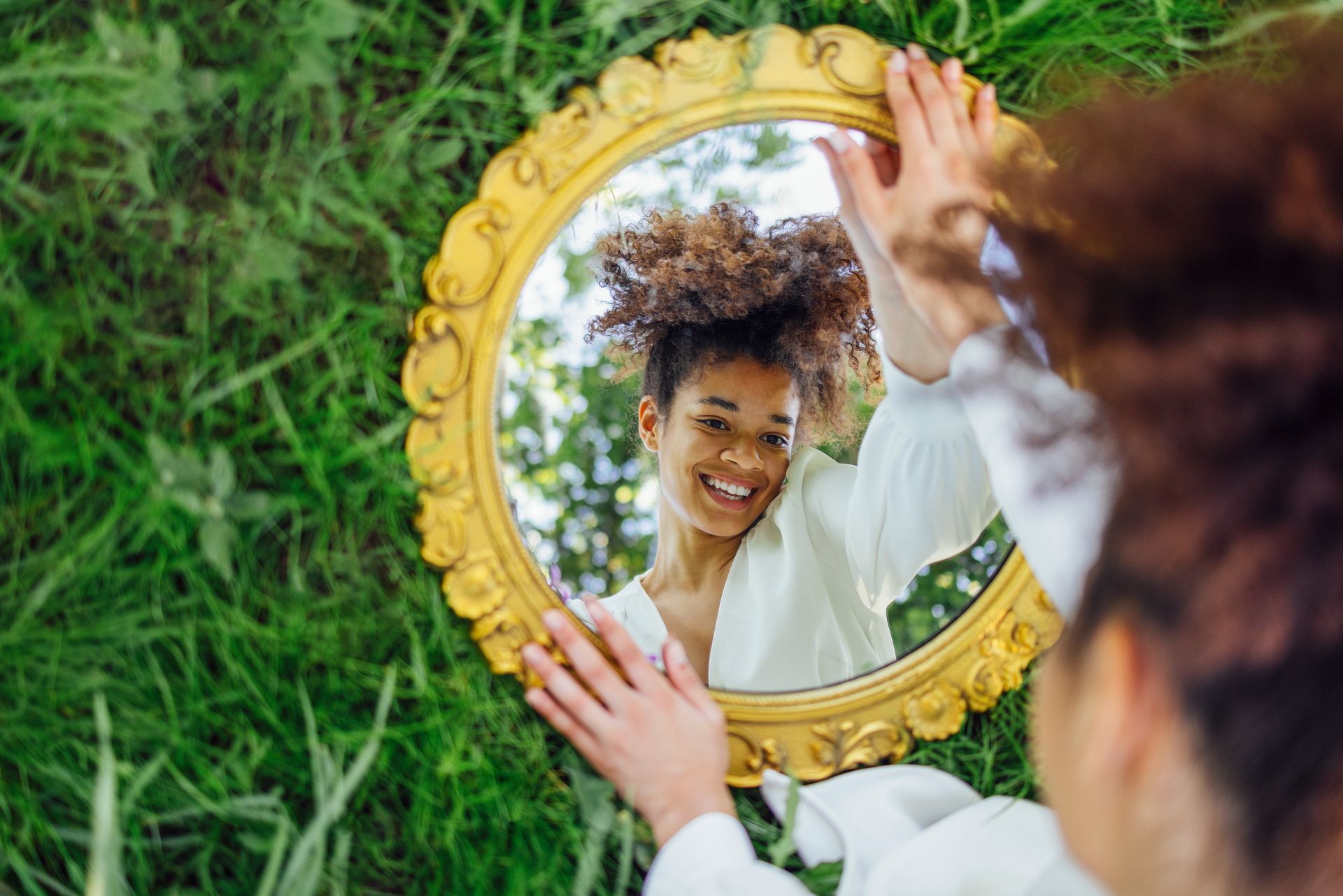 A woman is looking at her reflection in a mirror in the grass.