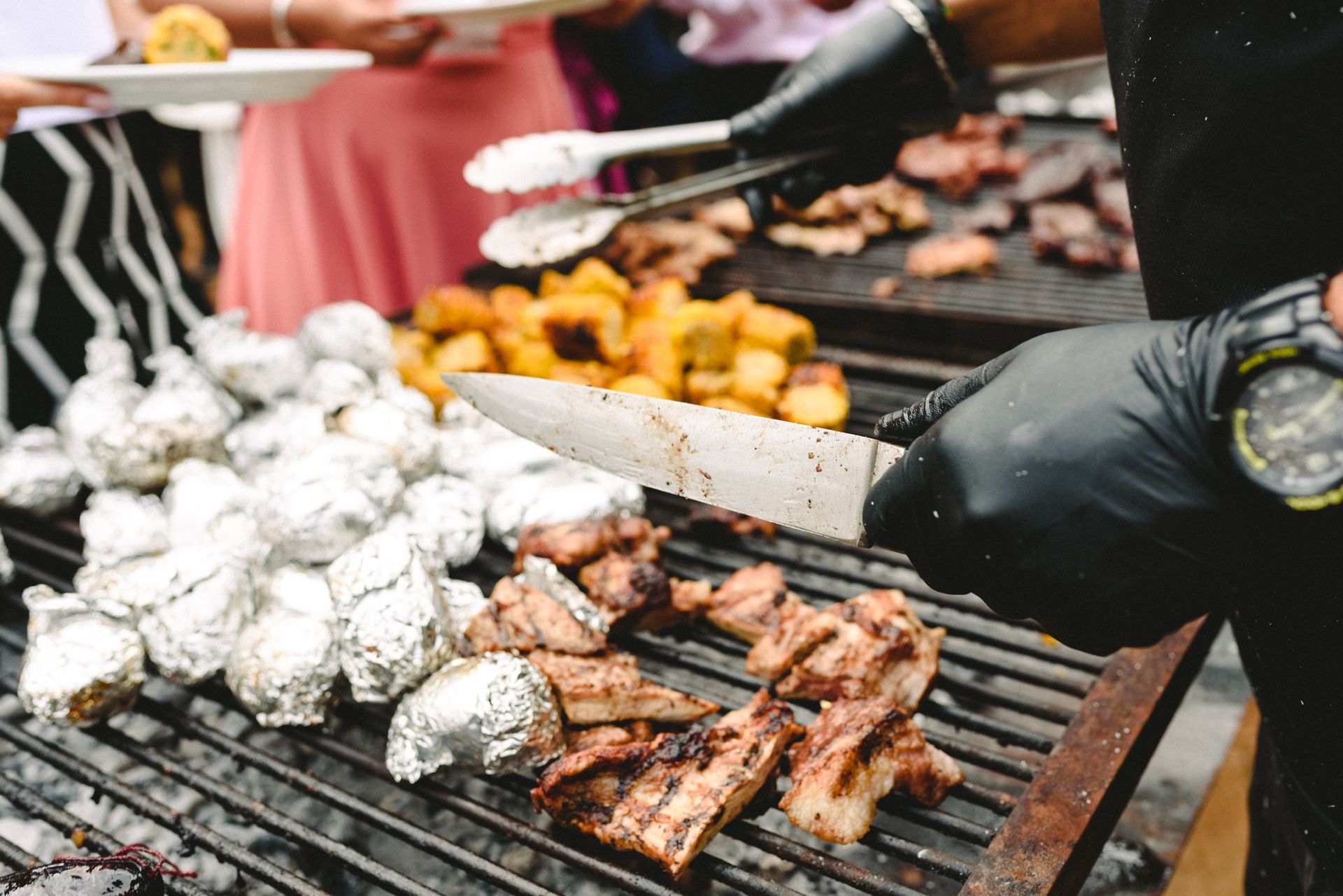 A person is cutting meat and potatoes on a grill.