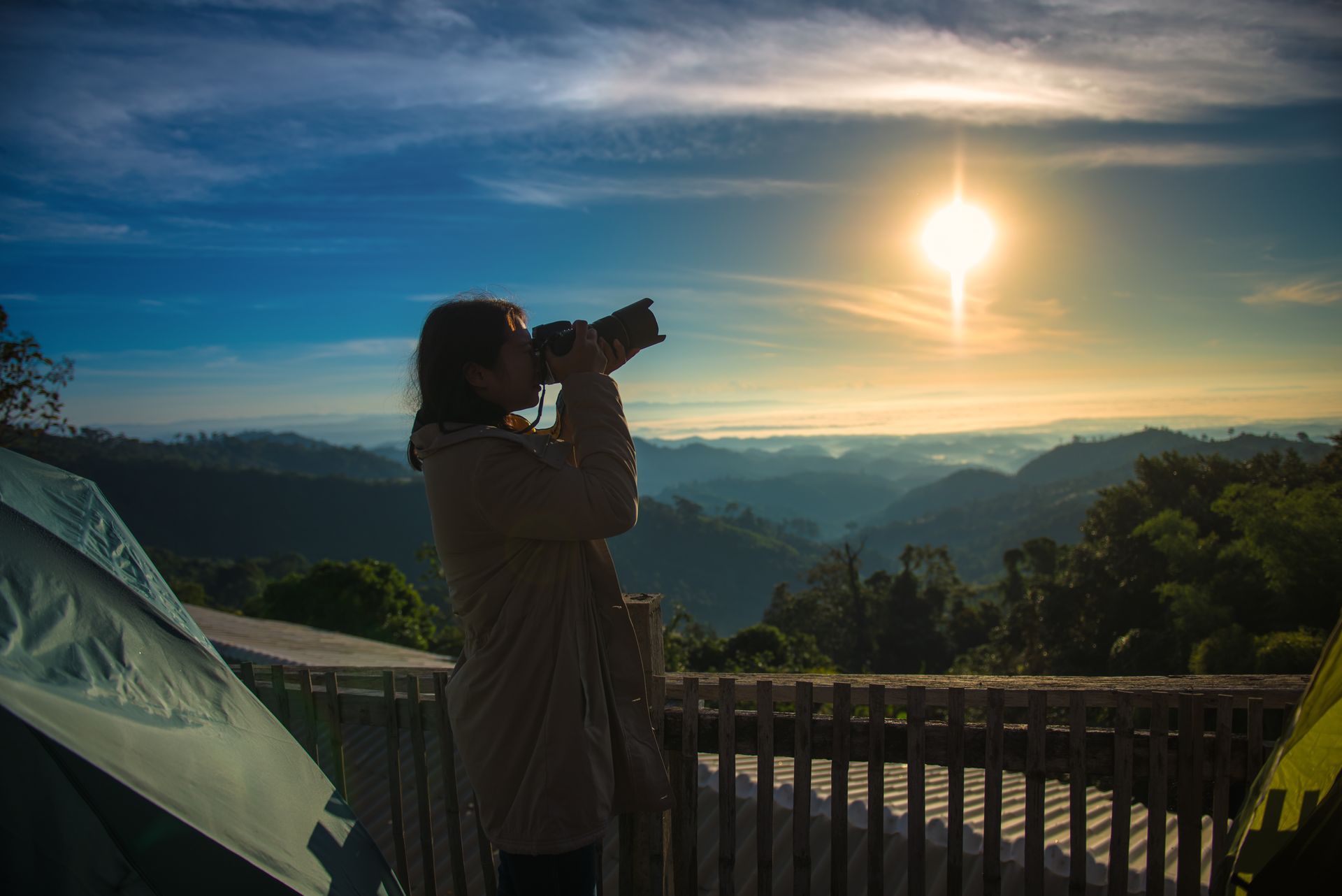 A woman is taking a picture of the sun rising over the mountains.
