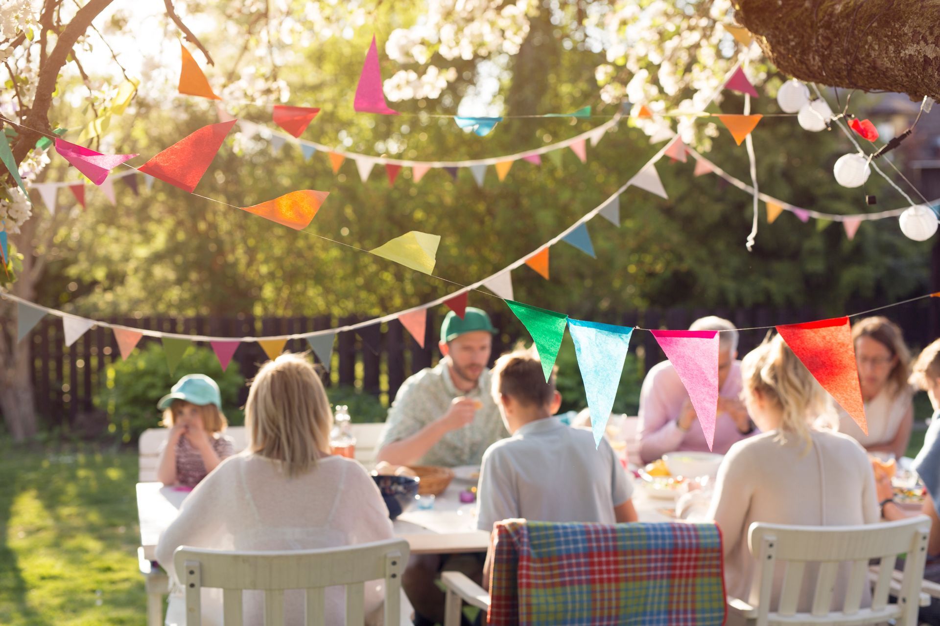 A group of people are sitting at a table with flags hanging from the trees.
