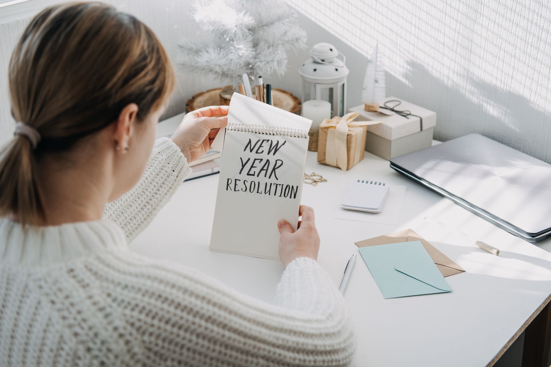 A woman is sitting at a desk holding a piece of paper that says `` new year resolution ''.