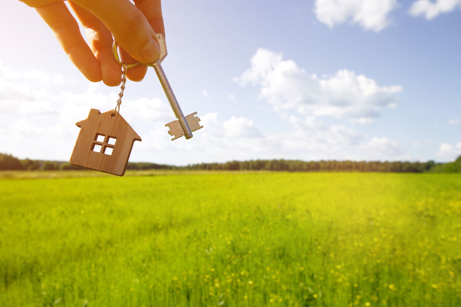 A person is holding a key with a house keychain in front of a field.