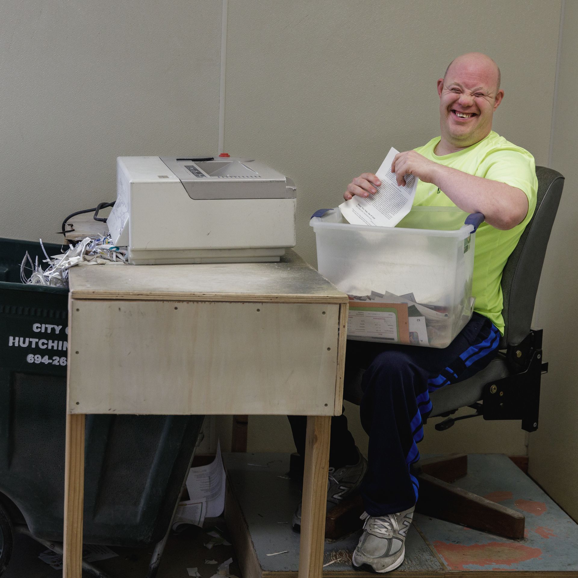 A man sits at a desk next to a trash can that says city hutchinson