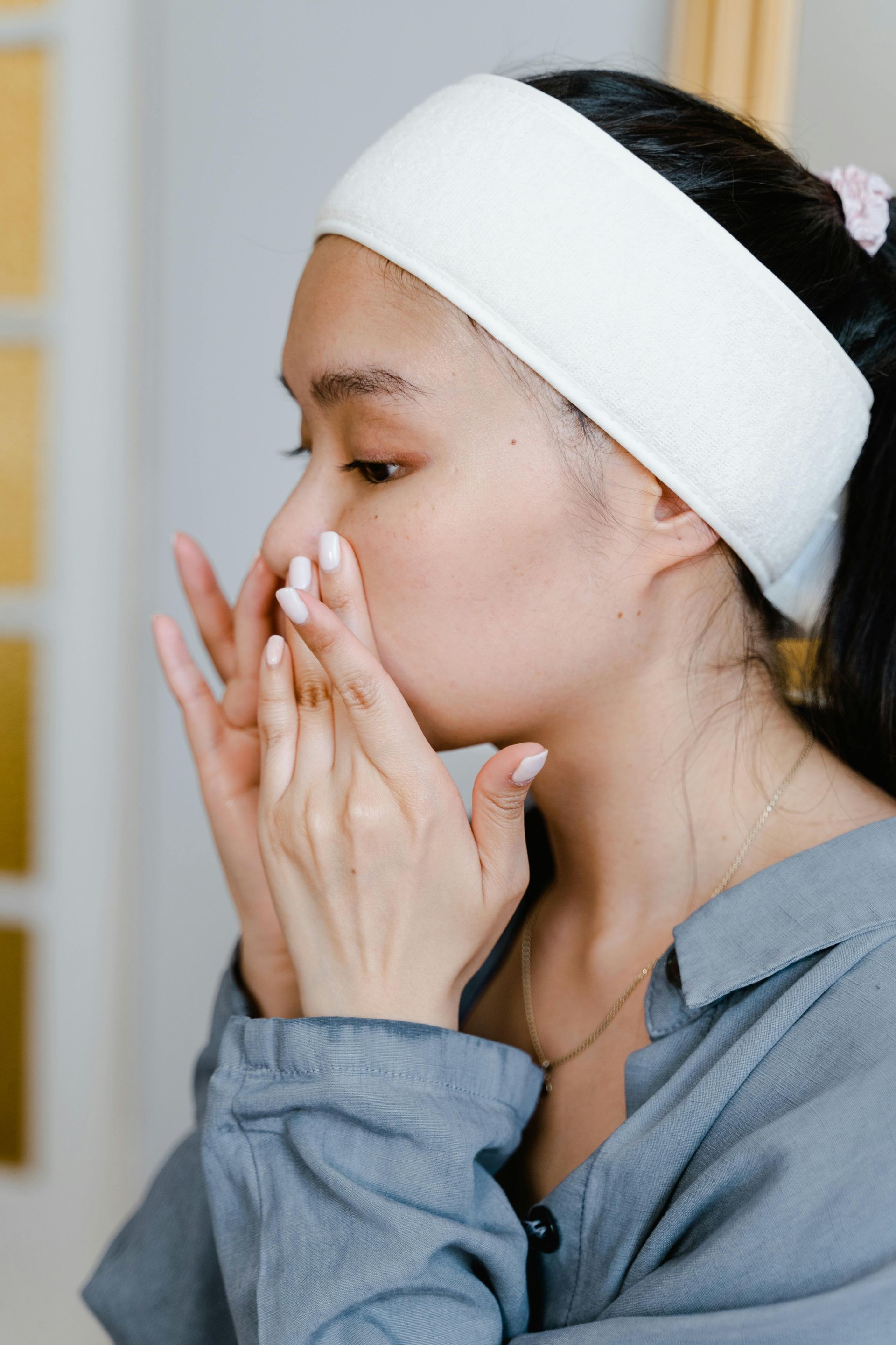Woman with white headband applying skincare to her nose and face indoors