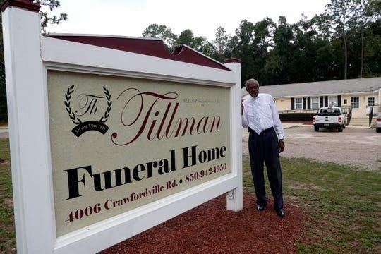 Sign for Tillman Funeral Home with a man standing nearby. Building in background.
