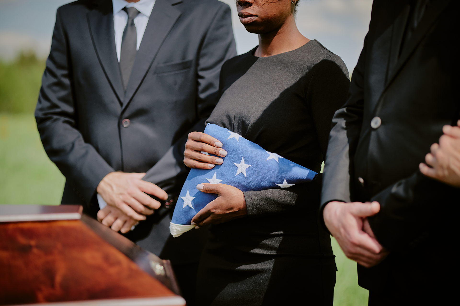 A woman is holding an american flag and a rose at a funeral.