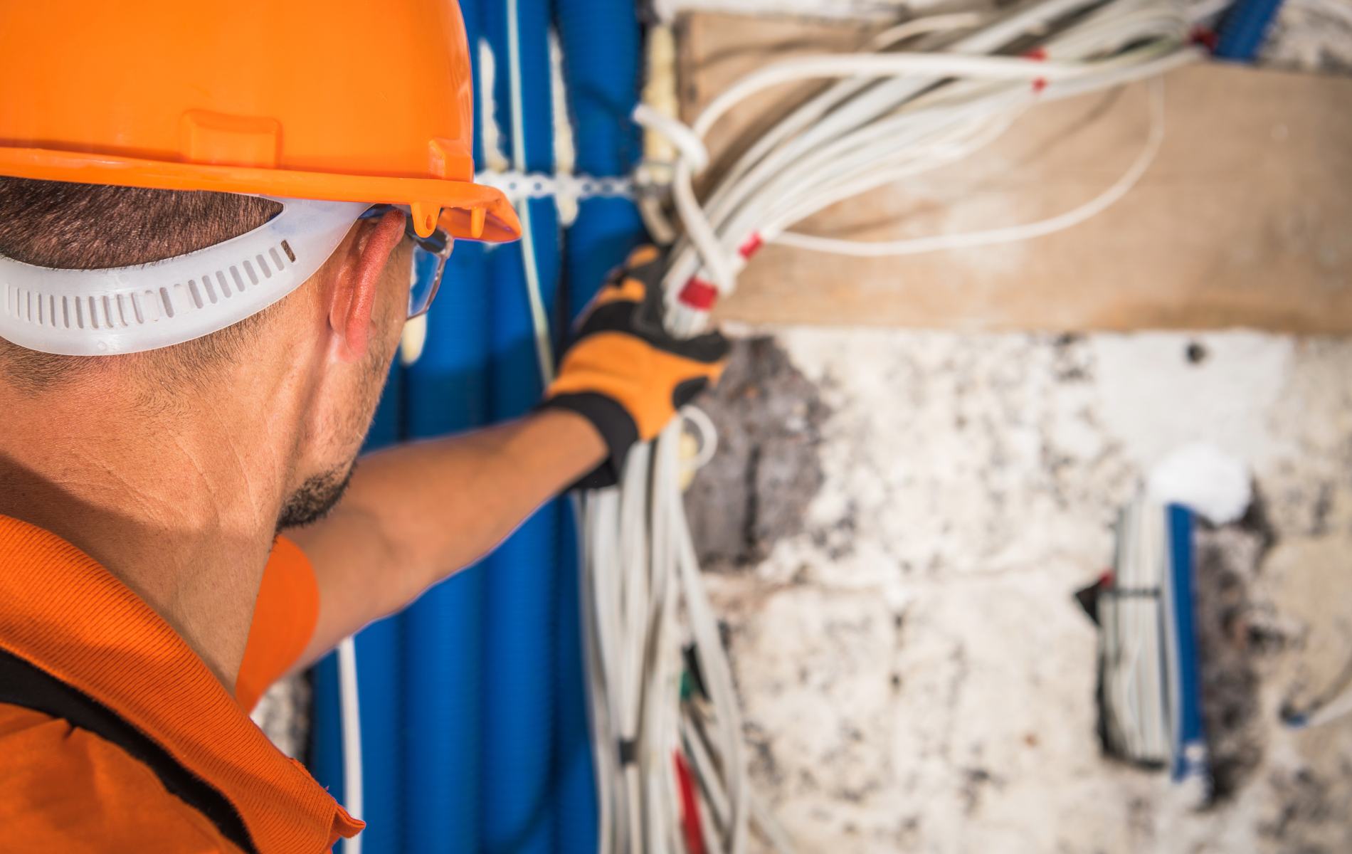 Electrician in orange gear working with electrical wires.