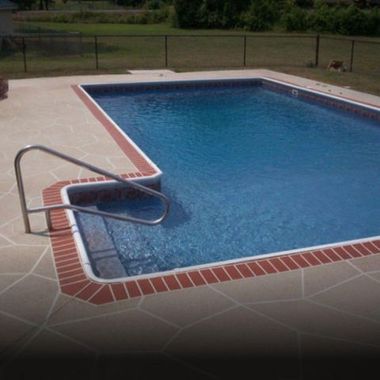 Rectangular swimming pool with brick trim and a gray stone patio. Handrail leads into shallow end.