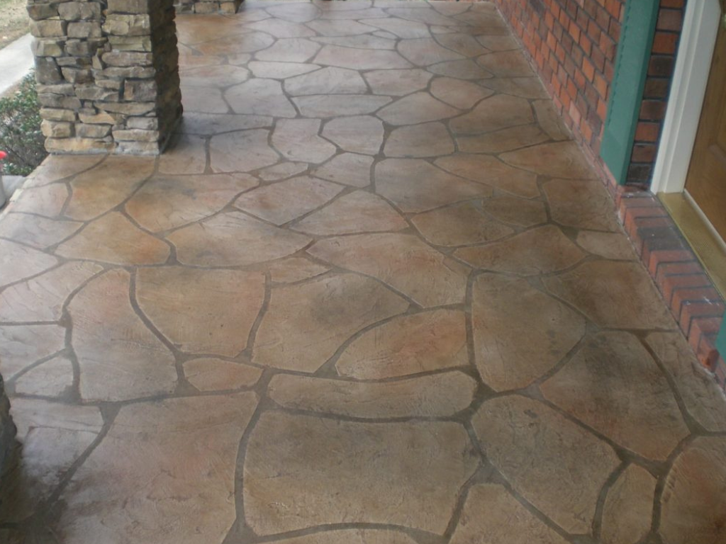 Stone-patterned concrete porch with dark grout lines, next to a brick wall and a stone column.