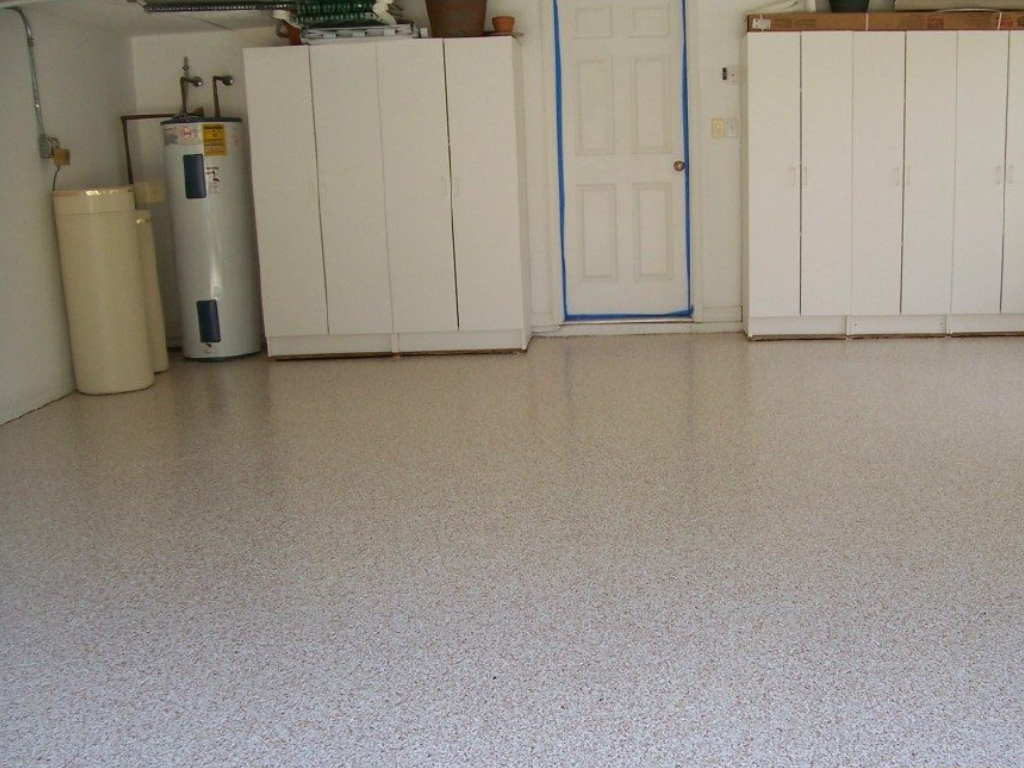 Garage with speckled epoxy floor, white cabinets, and water heater. Door frame is taped.