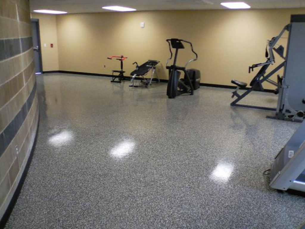 Gym with speckled gray floor and workout equipment: elliptical, weight machines, and bench. Beige walls.