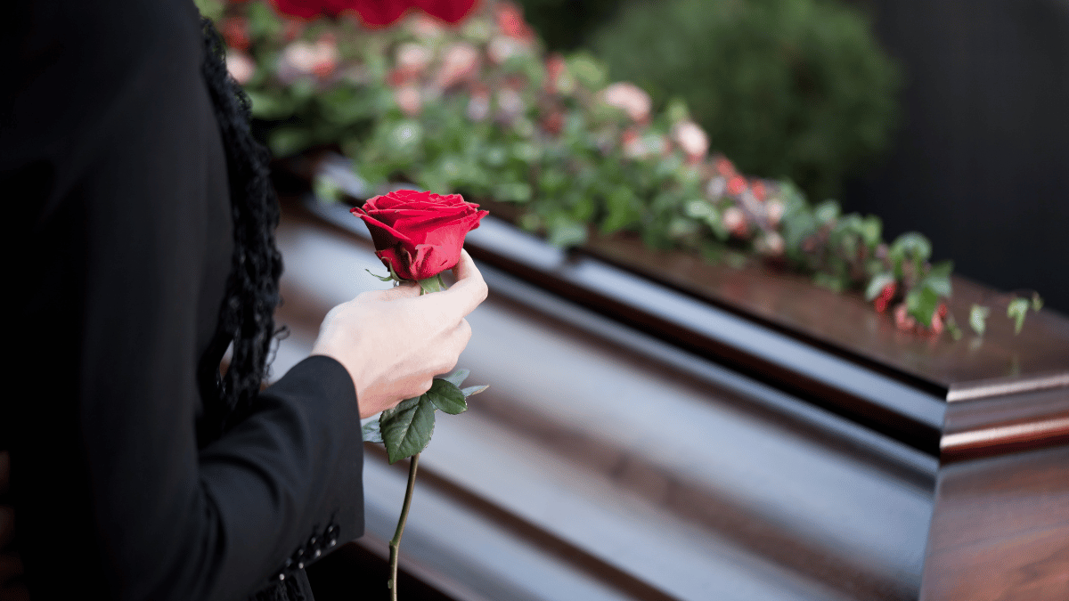International Funeral Service Southview Trenton NJ - Person holding red roses beside a polished casket at a funeral