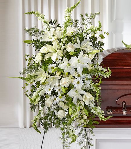 White floral funeral spray beside a polished wooden casket in a bright room