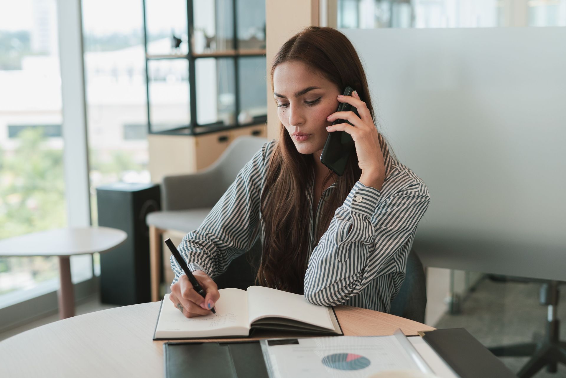 International Funeral Service Southview Trenton NJ - Woman on a phone call while writing in a notebook at a desk in a office.