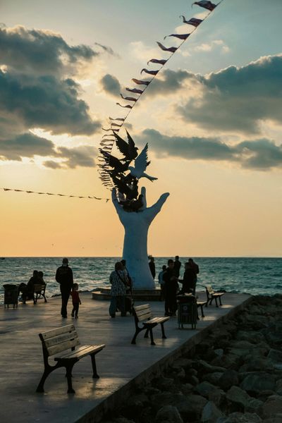 International Funeral Service Southview Trenton NJ - People on a seaside pier around a white sculpture at sunset.