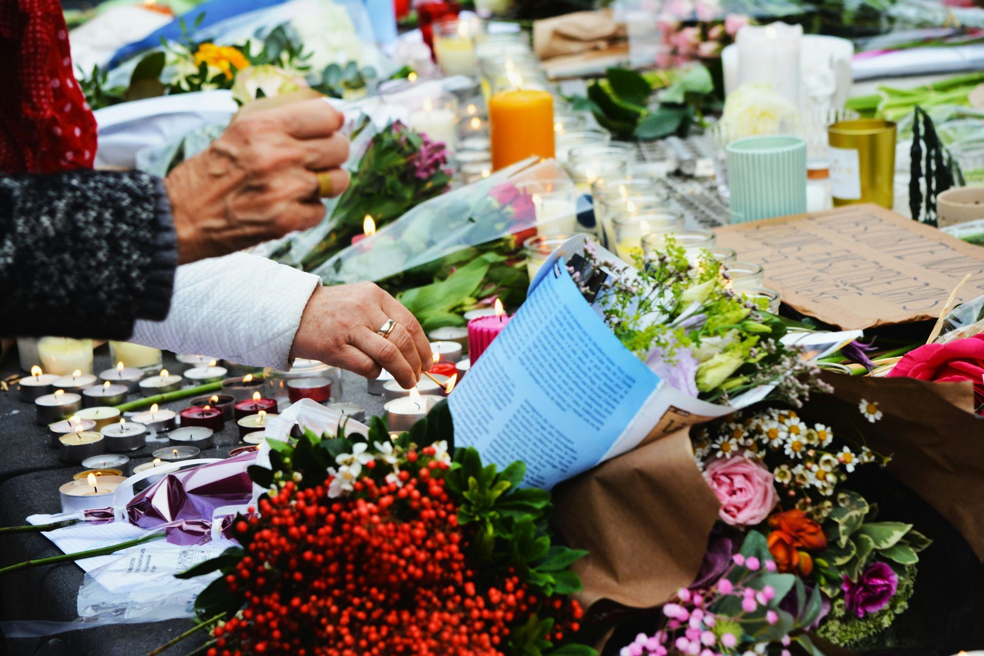 Hands arranging flowers and cards among bouquets and candles at a memorial table