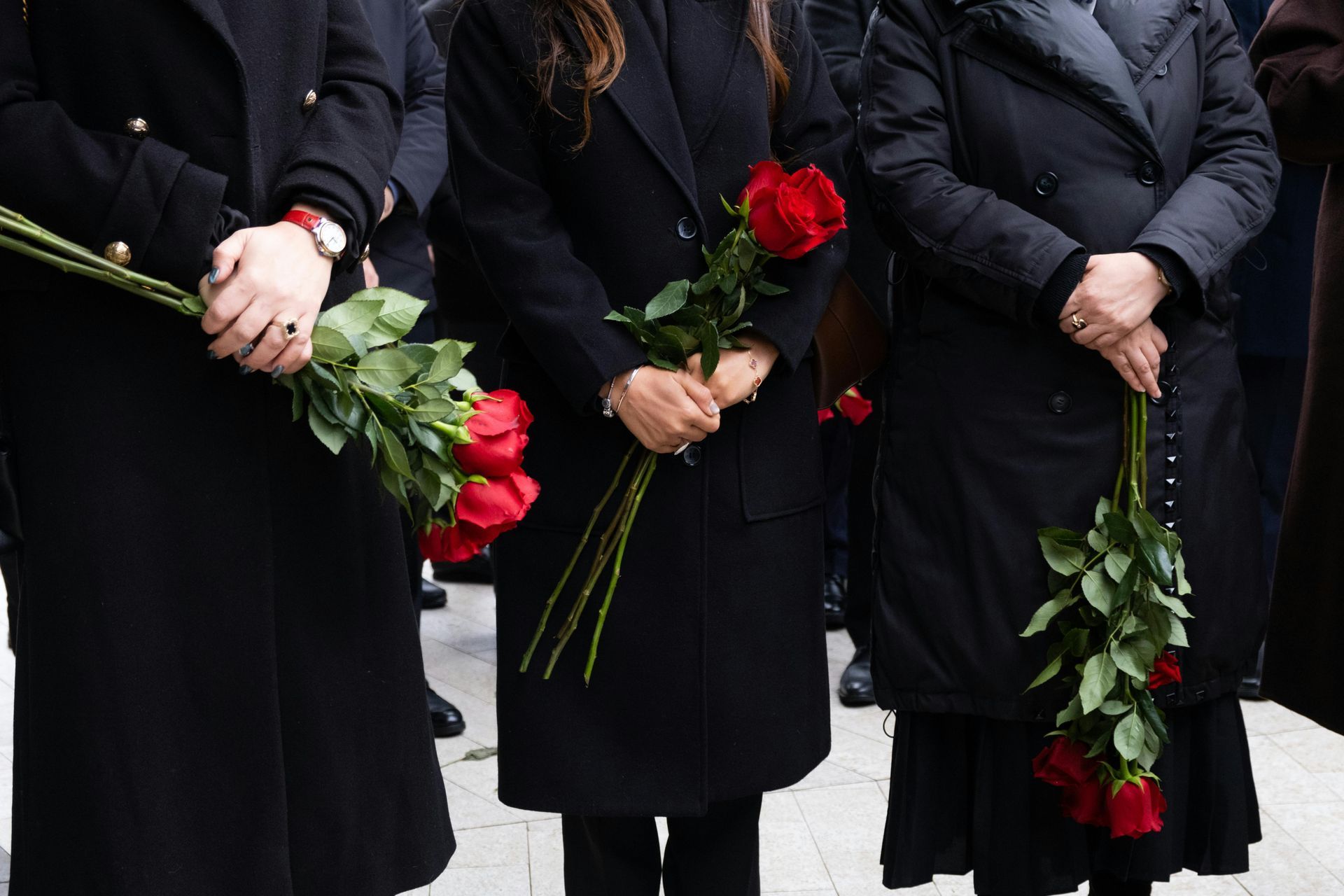 International Funeral Service Southview Trenton NJ - Three people in black coats holding red roses at a memorial.