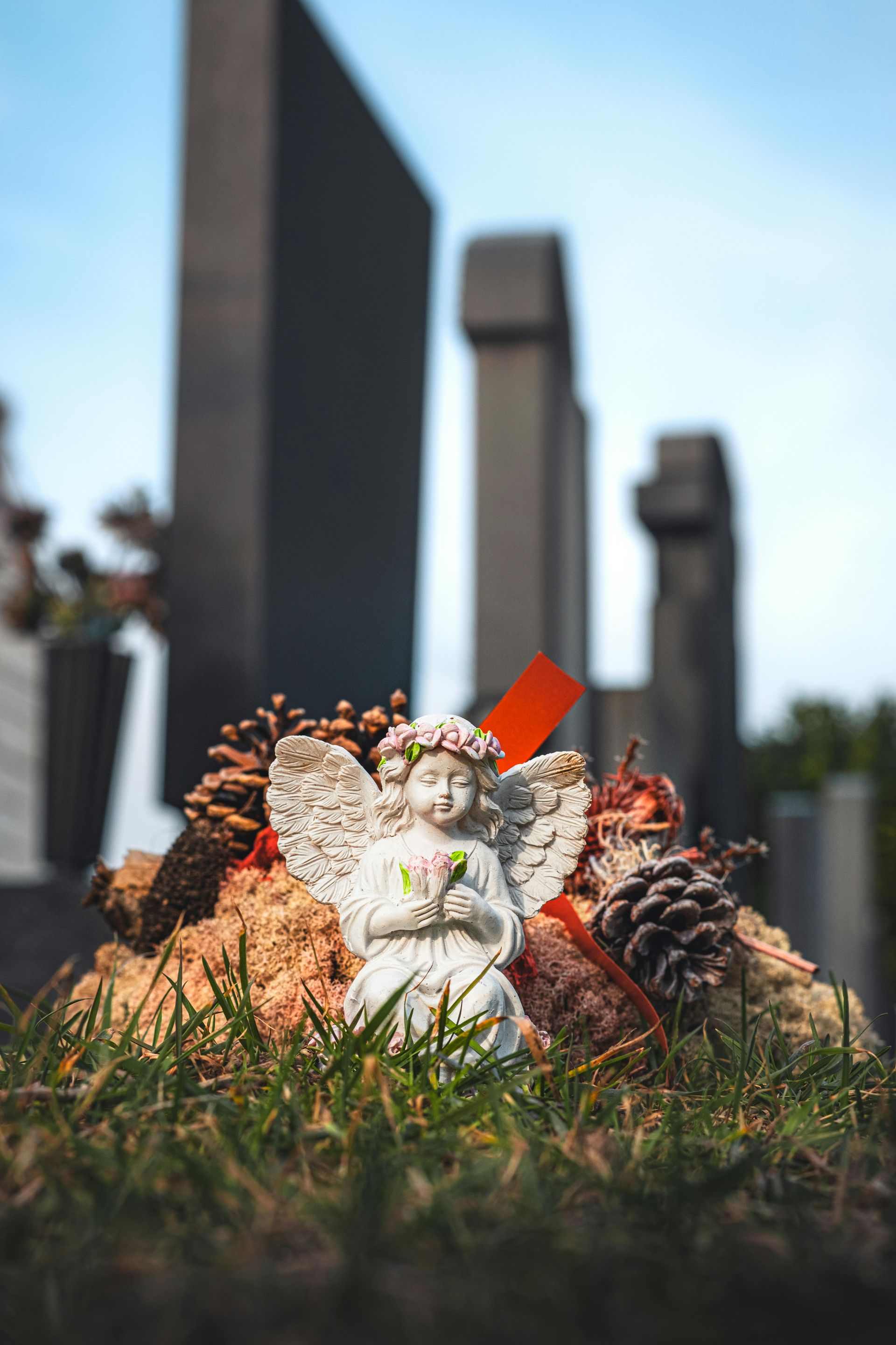 Small angel figurine on grass with blurred cemetery tombstones in the background