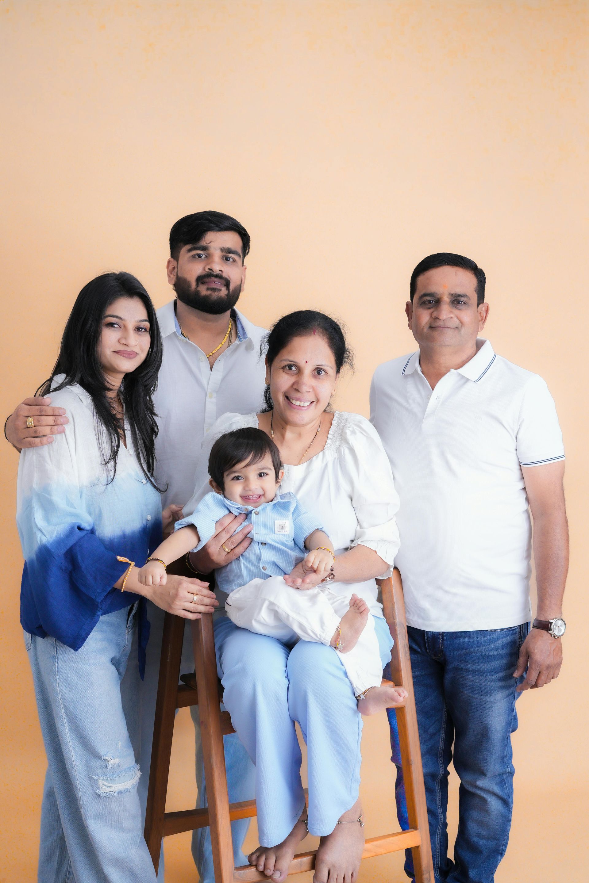 Five people posing indoors, seated and standing together against a peach wall.