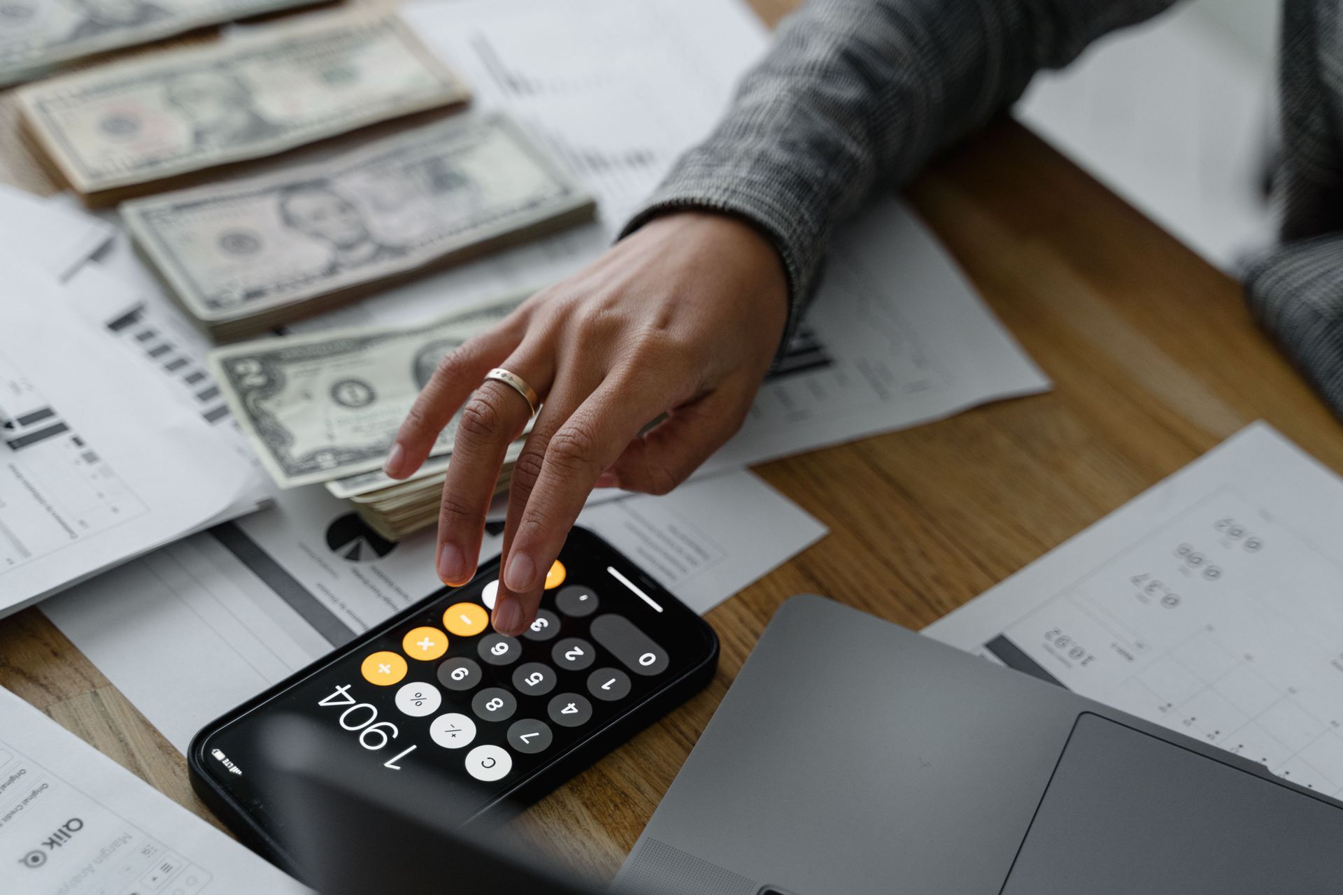 International Funeral Service Southview Trenton NJ - Hand using a calculator beside dollar bills, receipts, and a laptop.
