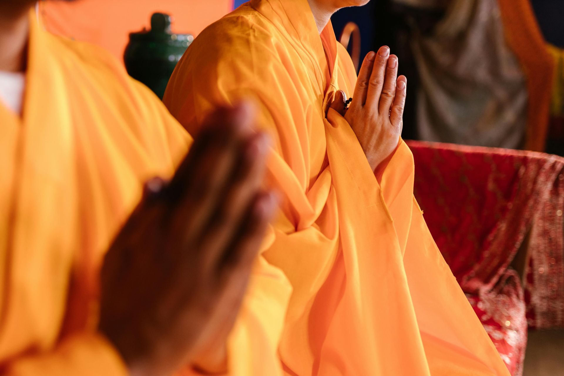 International Funeral Service Southview Trenton NJ - Hands folded in prayer, with people in orange robes seated indoors.