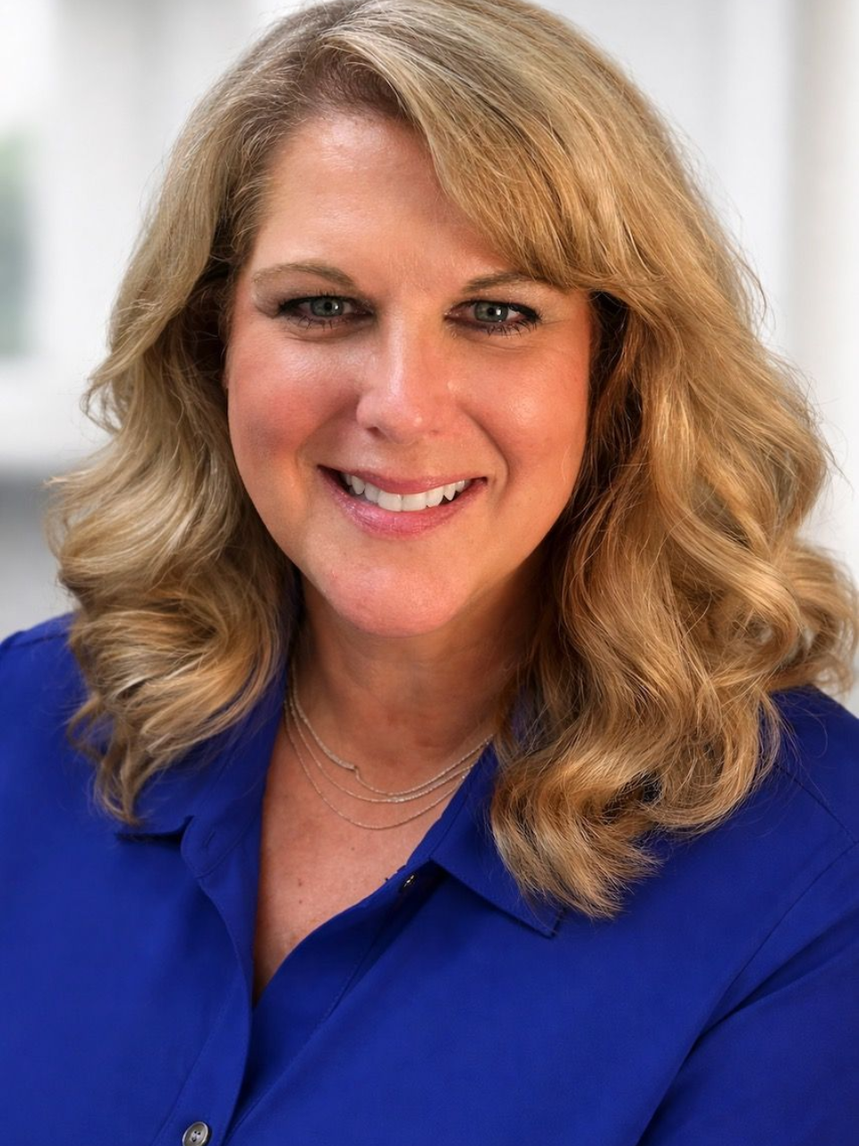 A woman in a blue shirt and black jacket is smiling for the camera.