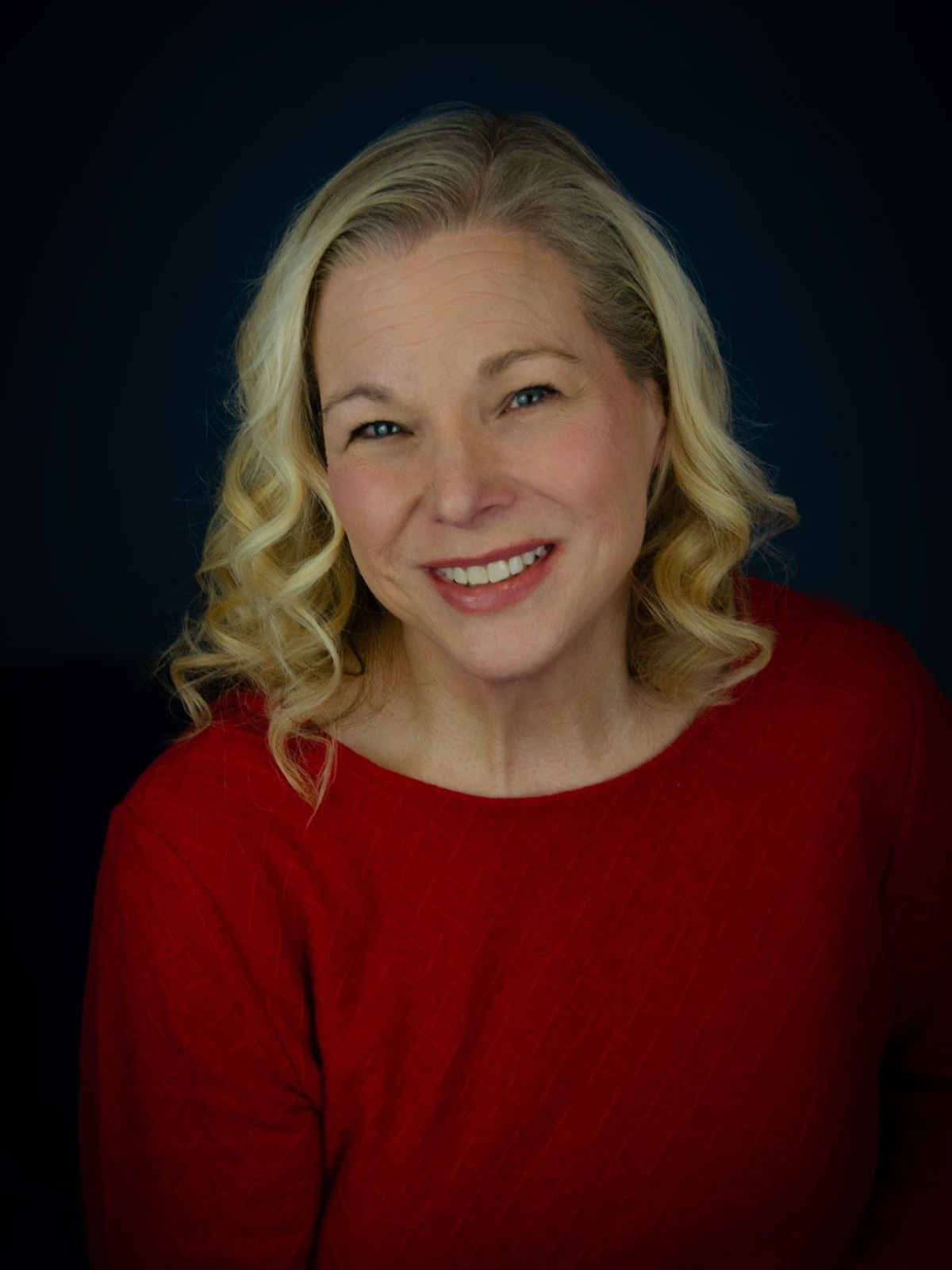 A woman with blonde hair is wearing a black shirt and a necklace.