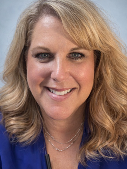 A woman in a blue shirt and black jacket is smiling for the camera.