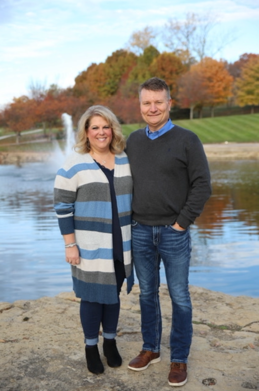 A man and a woman are standing next to each other in front of a pond.