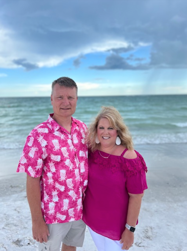 A man and a woman are posing for a picture on the beach.