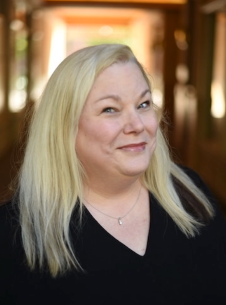 A woman with blonde hair and a black shirt is smiling for the camera.