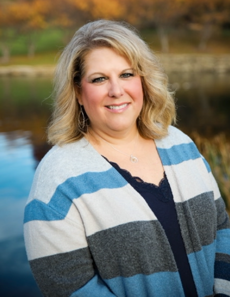A woman in a striped sweater is standing in front of a lake.
